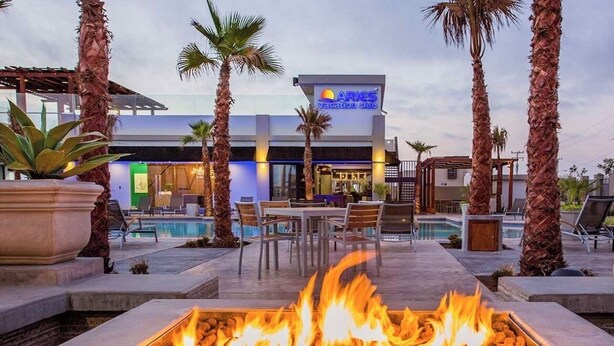 A fire pit in the foreground, a pool, and a building with a sign for 'ARIES Vacation Club' in the background. - Brand New Rosarito Home w/ Ocean Views (rosarito)