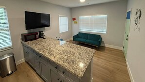 Eine Küche mit Granit Arbeitsplatten, einer Mikrowelle und einer Kaffeemaschine. Ein salbeengrünfarbenes Sofa und ein an der Wand befestigter Fernseher sind ebenfalls vorhanden.