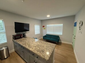 A kitchen with granite countertops, a microwave, and a coffee maker. There is a teal sofa and a TV mounted on the wall. - Cozy 2-Bedroom Apartment Near Wynwood • 2 Queen Beds & Full Kitchen (Miami)