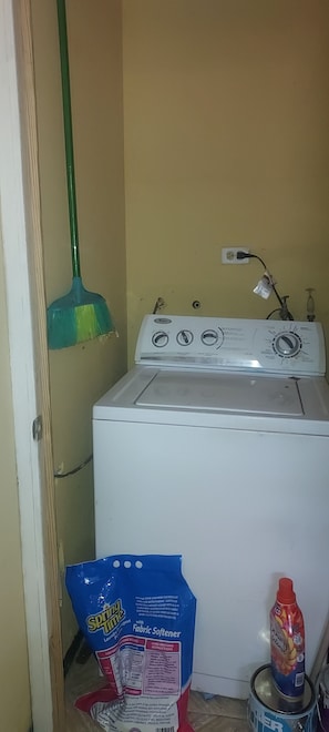 A laundry area with a washing machine, a mop, a bag of laundry detergent, and a bottle of dish soap.