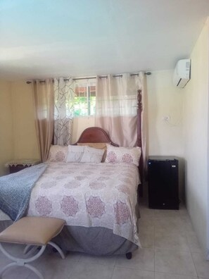 A bedroom with a bed, a bedside table, a chair, a small desk, and a heater.