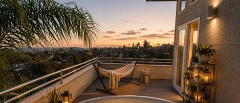Une terrasse sur le toit avec un jacuzzi, un hamac et une vue sur le paysage urbain au coucher du soleil.