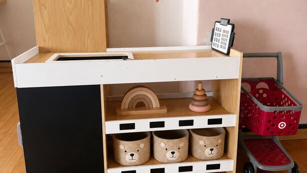 Ein Kinderspielbereich mit einem hölzernen Spieltisch, Aufbewahrungsboxen und einem Spielzeug-Ringschlangen-Stapler.