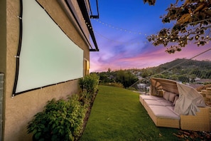 A backyard with a white screen, a wicker sofa, and a grassy area. - Panoramic Estate As Seen on 90 Day Fiancé (La Mesa)
