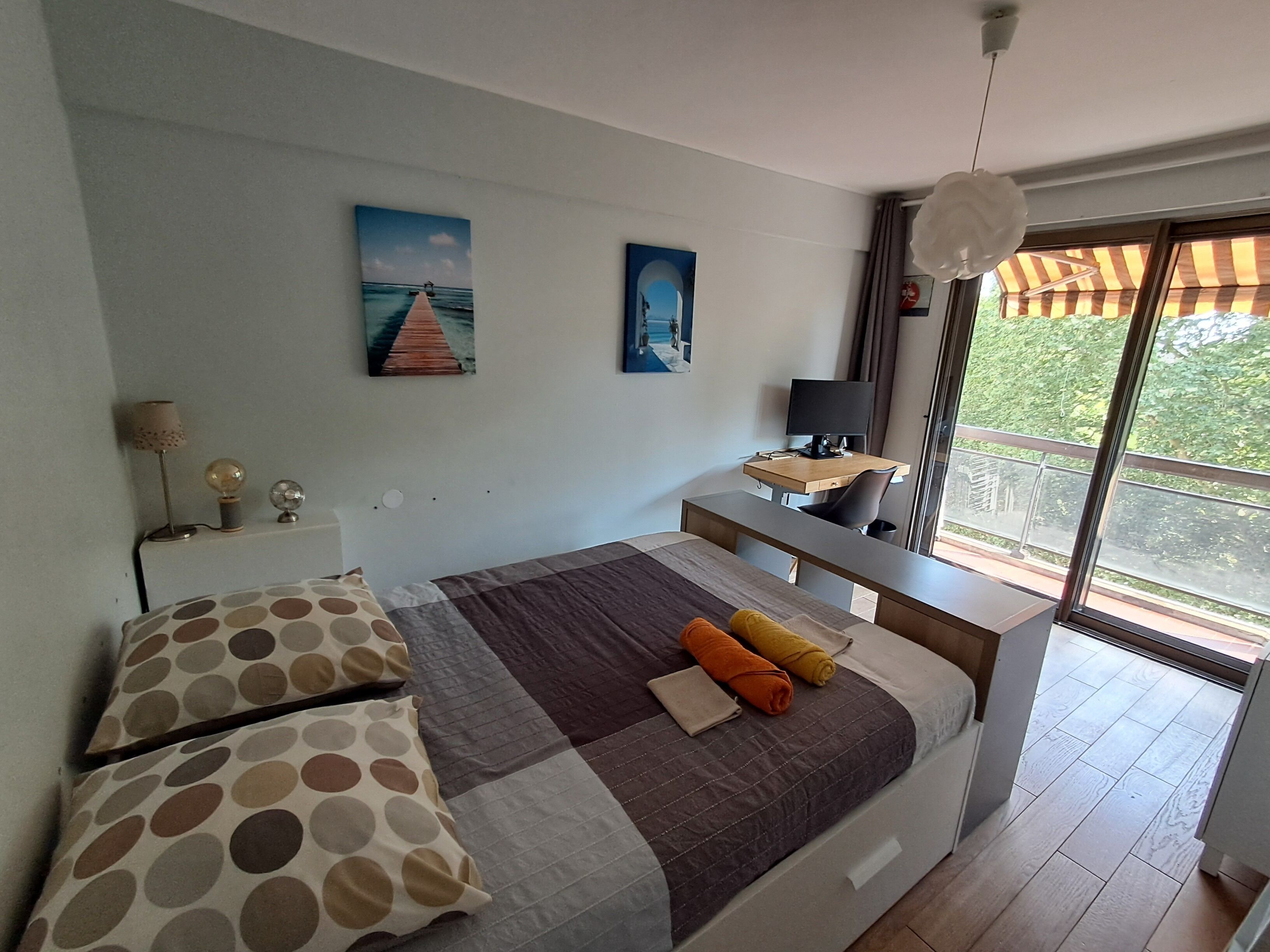 A modern bedroom with a large bed, a desk, and a view of greenery outside.