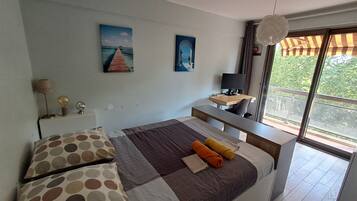 A modern bedroom with a large bed, a desk, and a view of greenery outside.