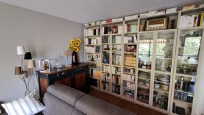 A living room with a sofa, a bookshelf filled with books and decorative items, and a coffee table with a vase of sunflowers. - Canal & Garonne Atmosphere – Live Like a True Toulousain (Toulouse)