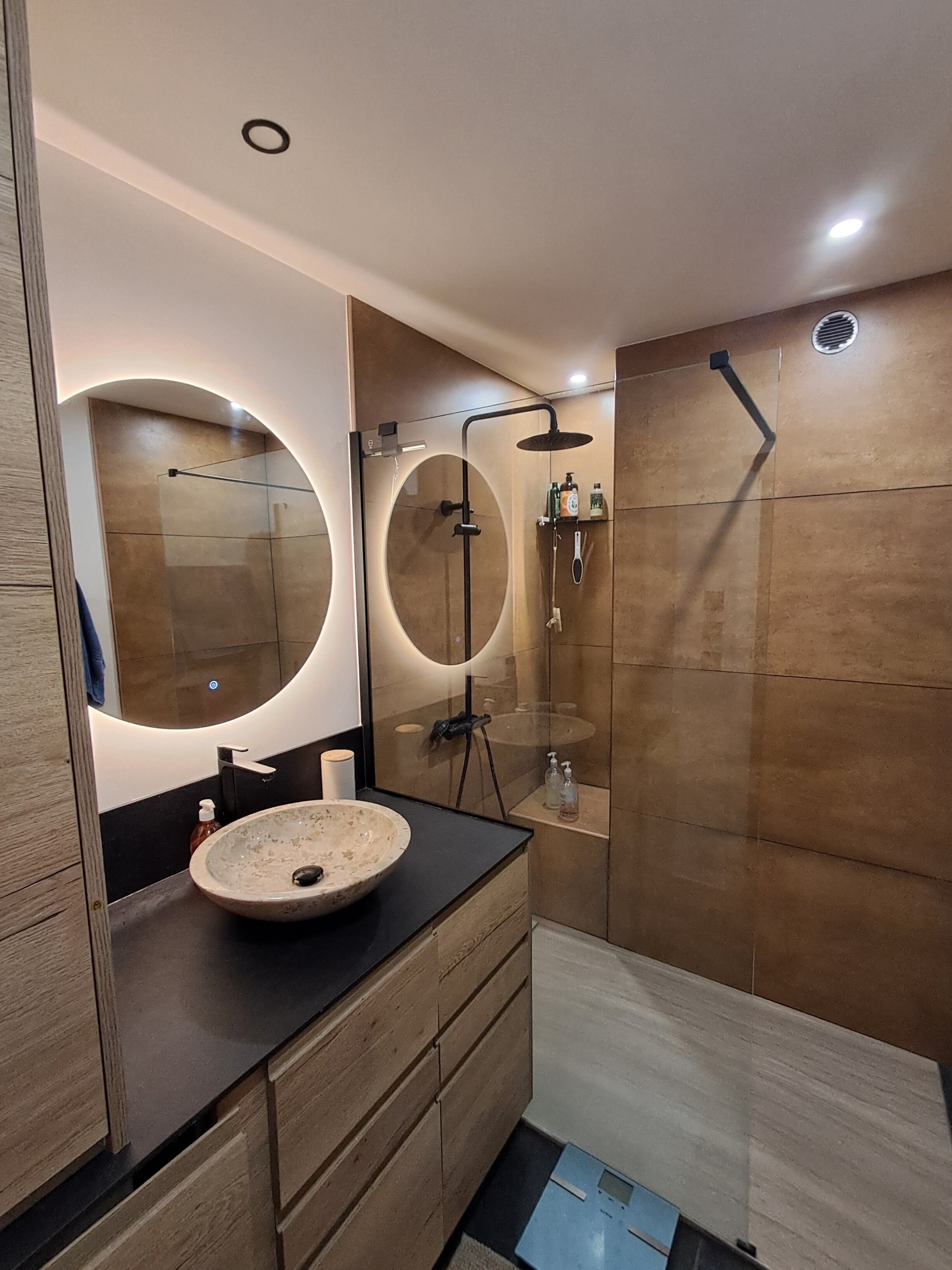 A modern bathroom with a round mirror, a sink, and a shower area.