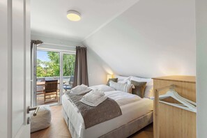 A bedroom with a bed, a wooden wardrobe, a hanging clothes rack, a bedside table with a lamp, and a view of an outdoor balcony. - HejU Beachfront Penthouse w/ 3 Balconies (Timmendorfer Strand)