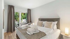 Ein Hotelzimmer mit Bett, Nachttisch, einem Fenster mit Vorhängen und Blick ins Freie.