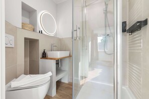 Ein modernes Badezimmer mit einer Duschkabine aus Glas, einem weißen Waschbecken und einem Spiegel mit runder Beleuchtung.