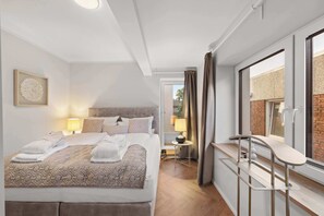 Ein modernes Hotelzimmer mit einem großen Bett, Nachttischlampen, einem Schreibtisch mit Stuhl und Blick ins Freie.