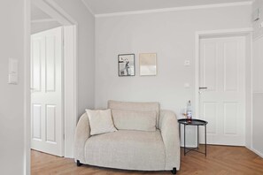 Ein Zimmer mit einem beigefarbenen Sofa, einem kleinen Tisch mit einer Flasche und zwei gerahmten Bildern an der Wand.