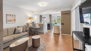 Ein modernes Wohnzimmer mit Sofa, Couchtisch, Fernseher und einer Küchenzeile im Hintergrund.