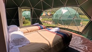 Una habitación tipo tienda de campaña con cama, una mesita y una ventana con vistas al exterior.