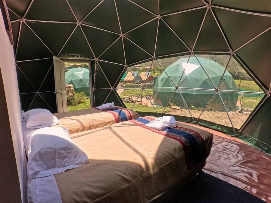 A tent-style room with a bed, a small table, and a window with a view of the outside.
