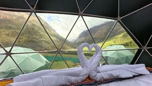 Una habitación con un diseño de ventana geométrico, una cama con una toalla en forma de corazón y vistas a un paisaje montañoso.