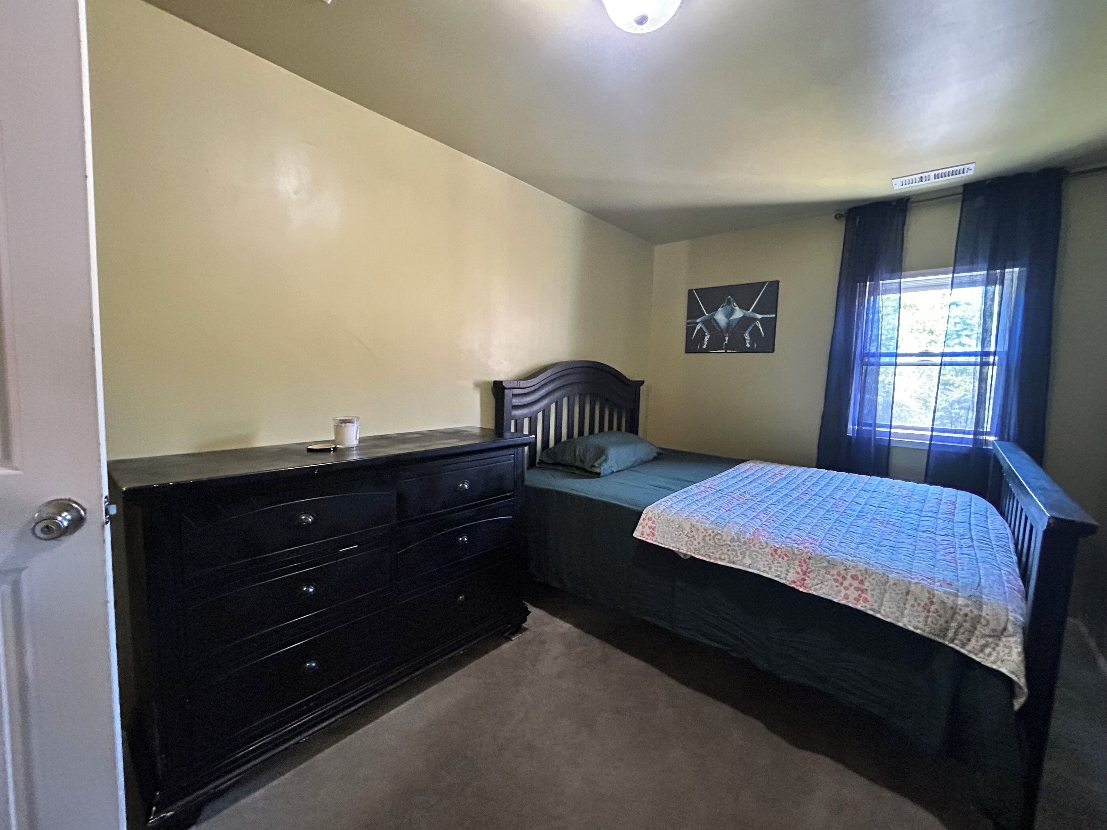 A bedroom with a bed, dresser, and a window with curtains.