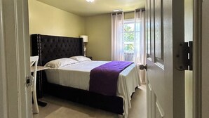Un dormitorio con cama, mesita de noche, silla y ventana con cortinas.