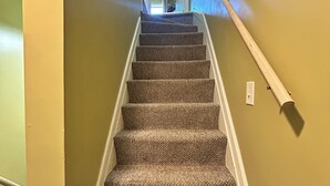 Una escalera alfombrada con barandilla, que conduce a un vano abierto en la parte superior.
