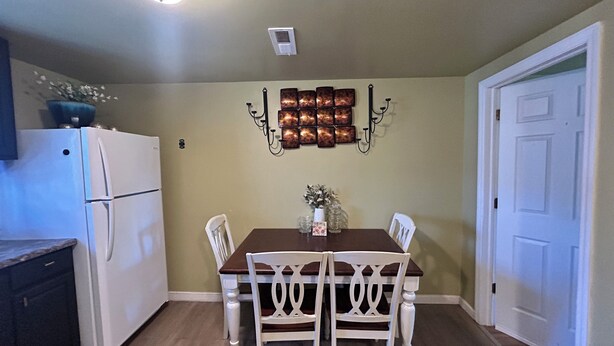 Un comedor con mesa, sillas, refrigerador y luces fijadas a la pared.