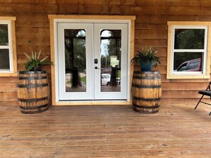 A wooden building with a double door, two potted plants, and a chair. - Float the river Historic 1916 Saddle Store with covered porchMammoth Spring Ar (Mammoth Spring)