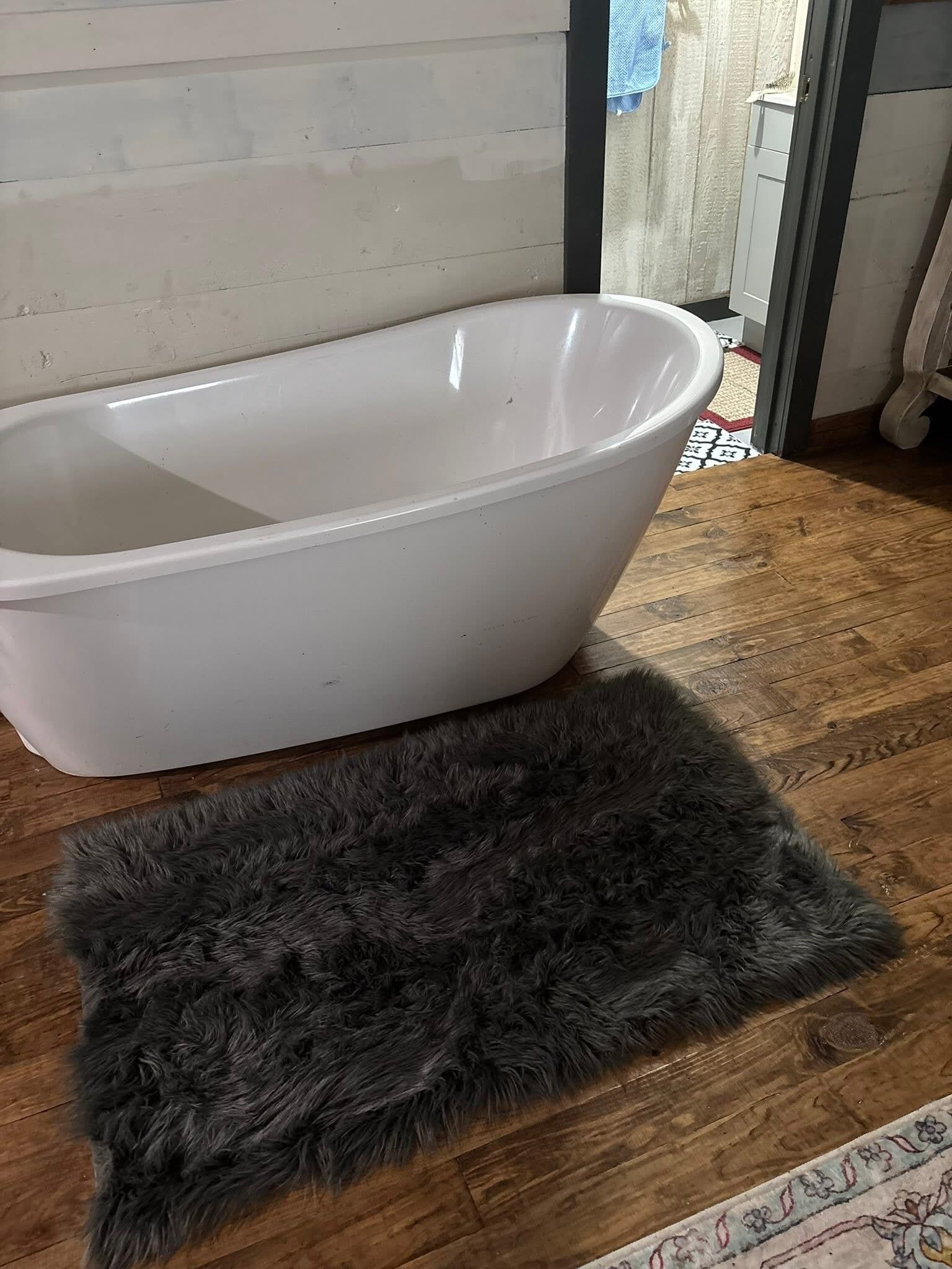 Une baignoire, un tapis épais et sombre à poils longs, un plancher en bois et un tapis à motifs.