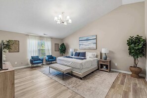 A bedroom with a large bed, a desk, a chair, a TV, and a plant.