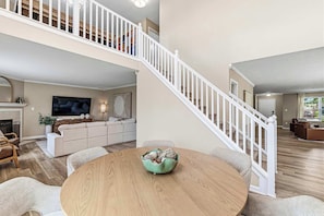 A spacious living area with a high ceiling, a staircase, a fireplace, and a large flat-screen TV.