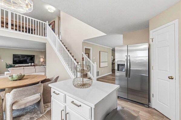 A modern kitchen with a stainless steel refrigerator, white cabinetry, and a dining area with a round table and chairs.