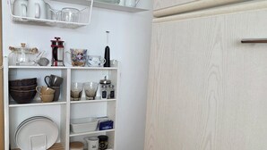 Una cocina con armarios blancos, estantes con vajilla, una cafetera y un taburete.