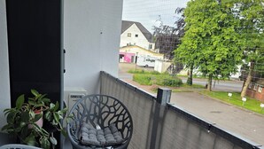 Un balcón con dos sillas, una planta en maceta y vista a una calle residencial.