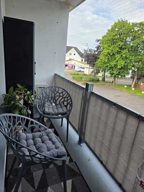 A balcony with two chairs, a potted plant, and a view of a residential street. - Vacation rental near Sylt with a balcony and parking in the heart of Leck (Leck)