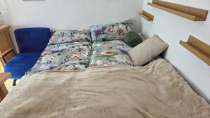 Una cama con edredón floral, una silla azul y cabeceros de madera.