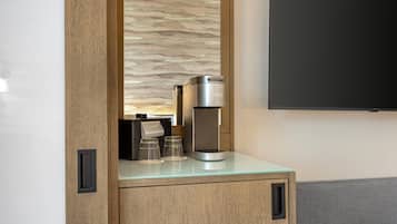 A modern kitchenette with a coffee maker, two glasses, and a small cabinet.