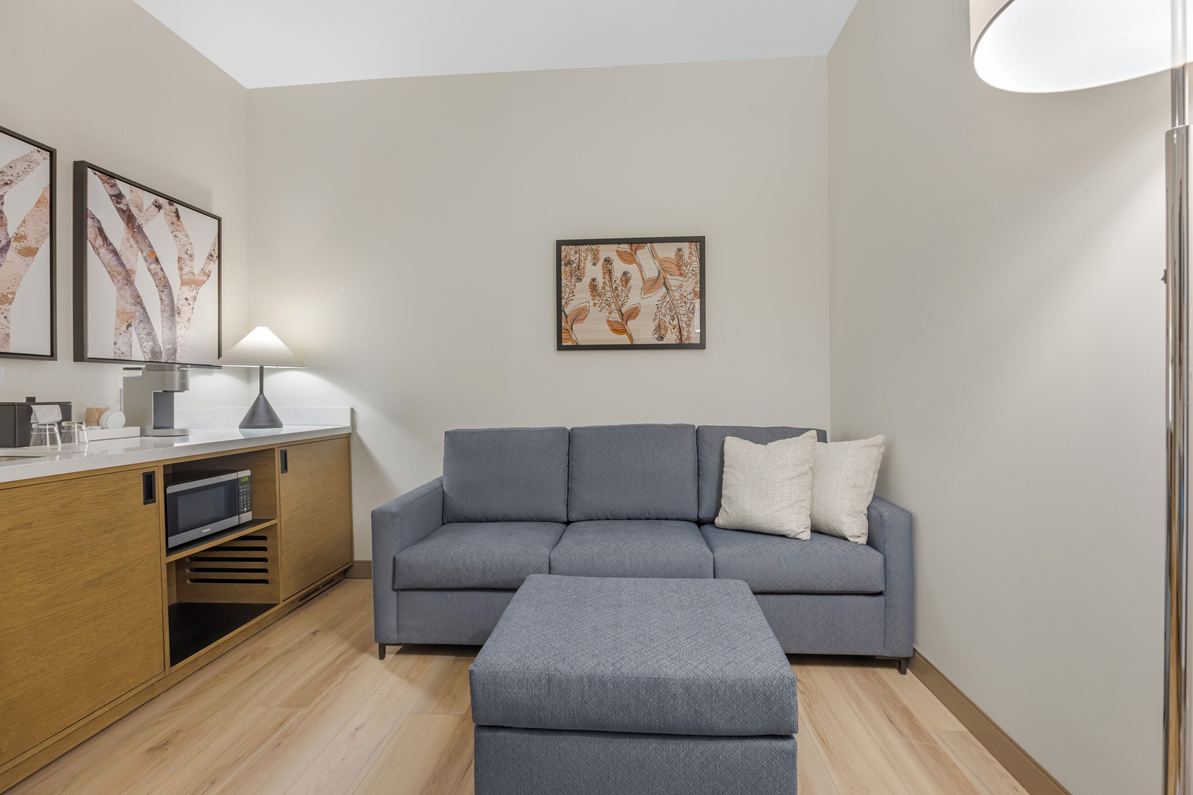 A modern living room with a grey sofa, a wooden cabinet, and a dining area.