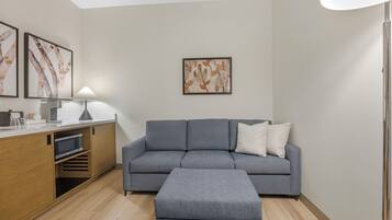 A modern living room with a grey sofa, a wooden cabinet, and a dining area.