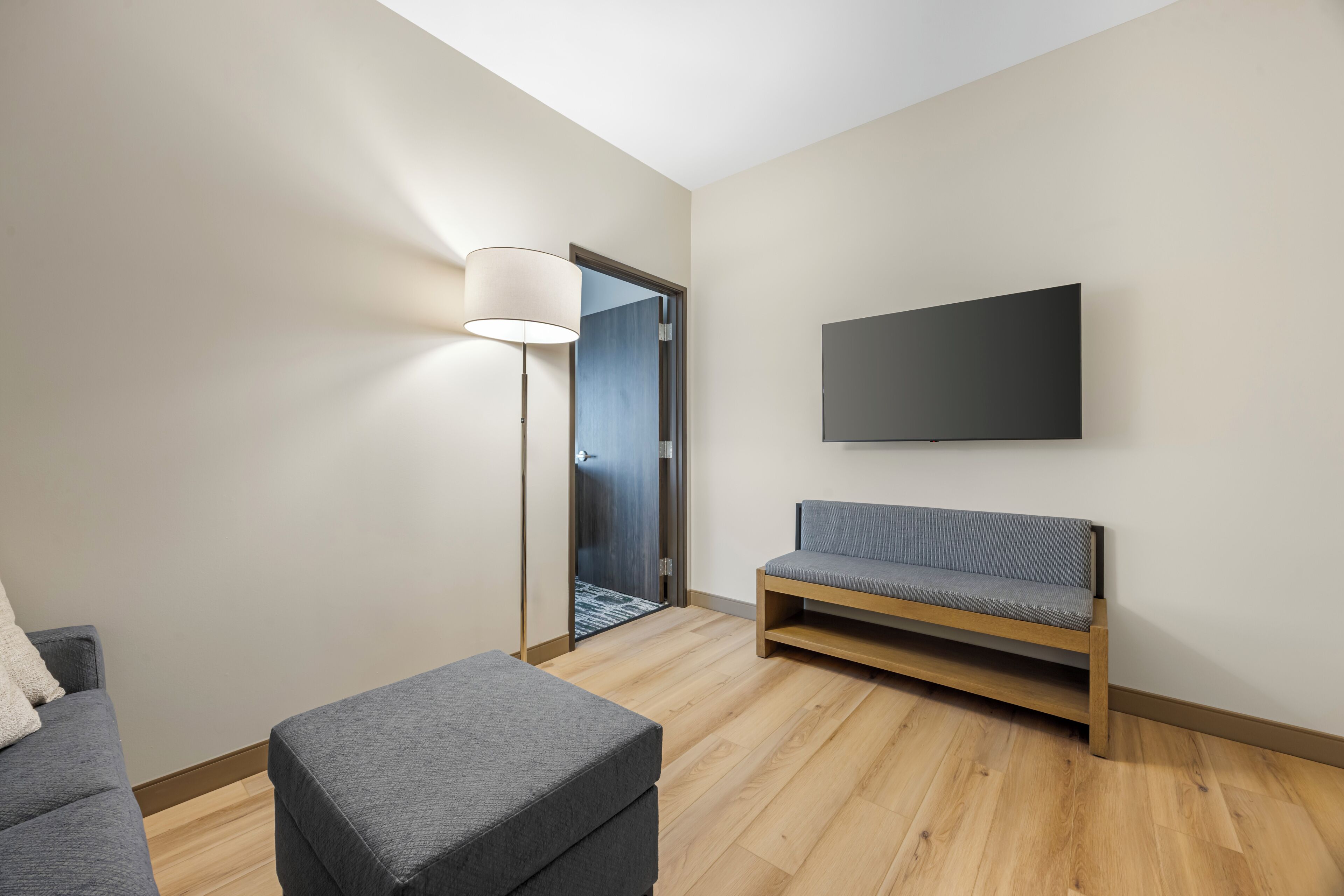 A modern living room with a sofa, ottoman, and a flat-screen TV mounted on the wall.