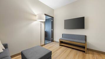 A modern living room with a sofa, ottoman, and a flat-screen TV mounted on the wall.