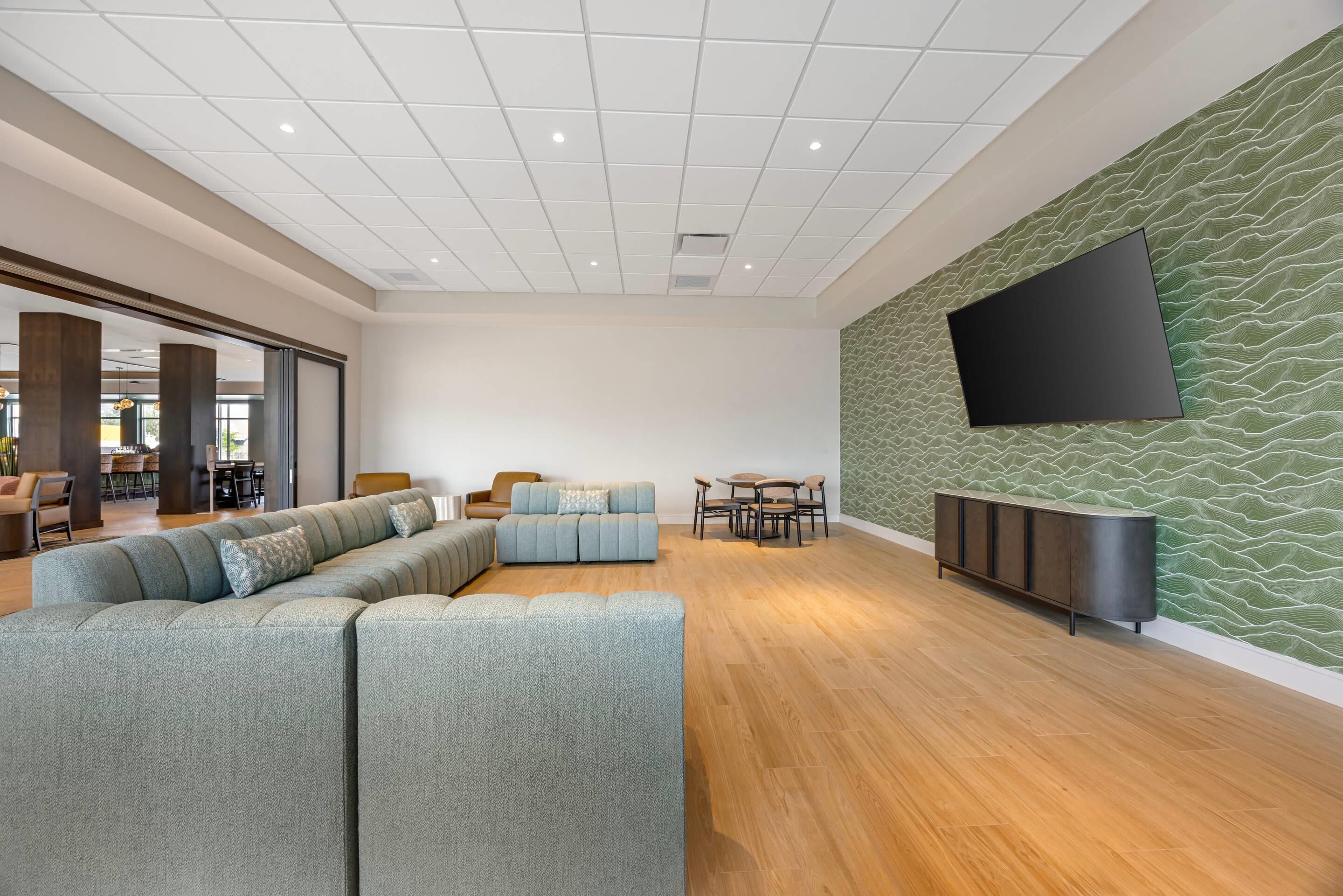 A modern lounge area with a sectional sofa, a dining table with chairs, and a flat-screen TV mounted on a textured wall.