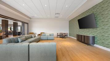 A modern lounge area with a sectional sofa, a dining table with chairs, and a flat-screen TV mounted on a textured wall.