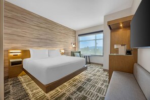 A hotel room with a large bed, a desk, a chair, a TV, and a window with a view.