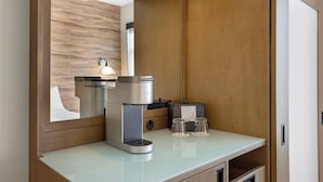 A modern kitchenette with a built-in coffee maker, a mirror, and a small table with glasses.
