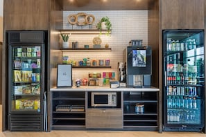 Un quiosco autoservicio con máquina de café, opciones de bocadillos y una pantalla digital para realizar pedidos.