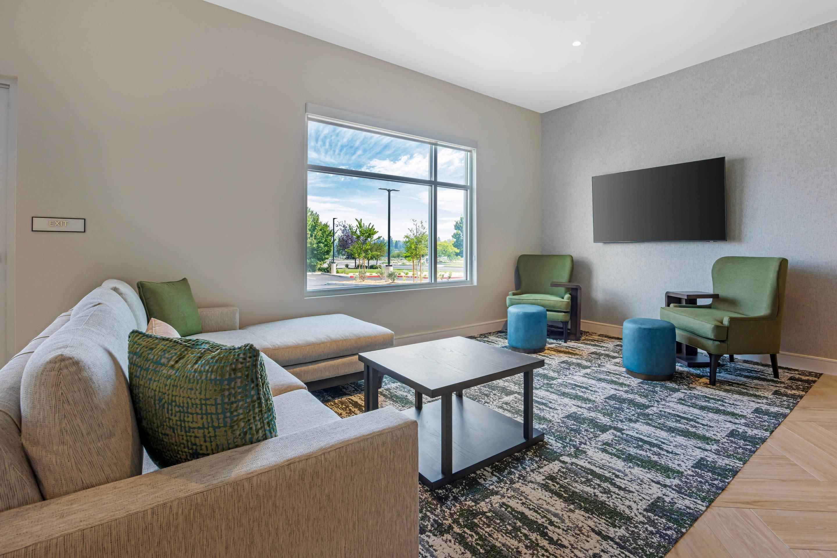 Una sala de estar moderna con un sofá, sillas, una mesa de centro y un amplio ventanal con vistas al exterior.