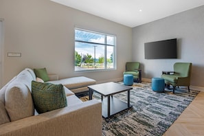 Una sala de estar moderna con un sofá, sillas, una mesa de centro y un amplio ventanal con vistas al exterior.