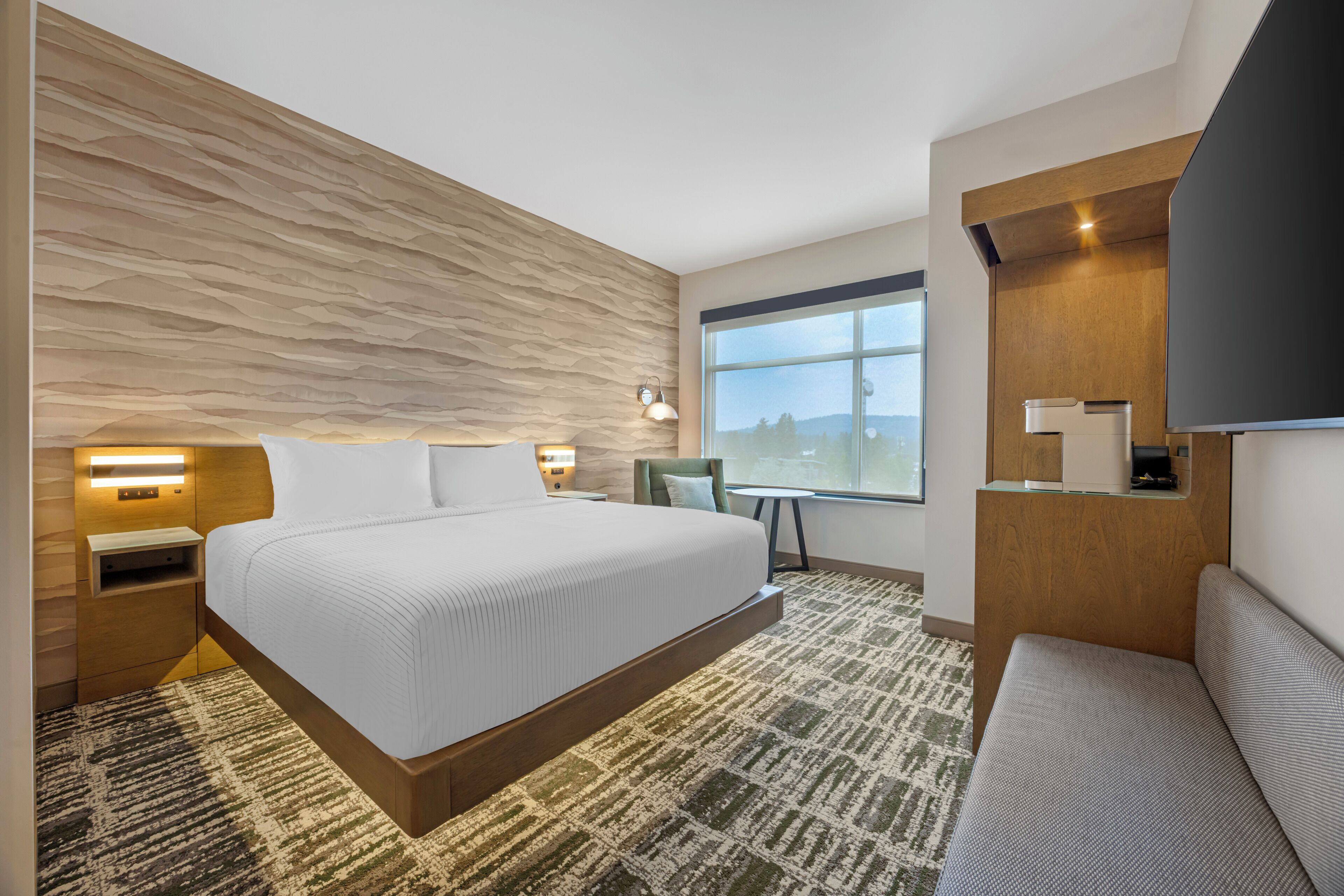 A modern hotel room with a large bed, a desk, a chair, and a TV.