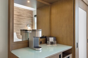 Un baño moderno con cafetera integrada, un espejo y un lavabo de vidrio.