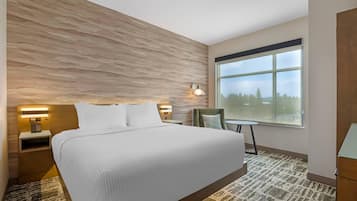 A hotel room with a large bed, a nightstand with a phone, a wall-mounted lamp, and a view of the outdoors through a large window.