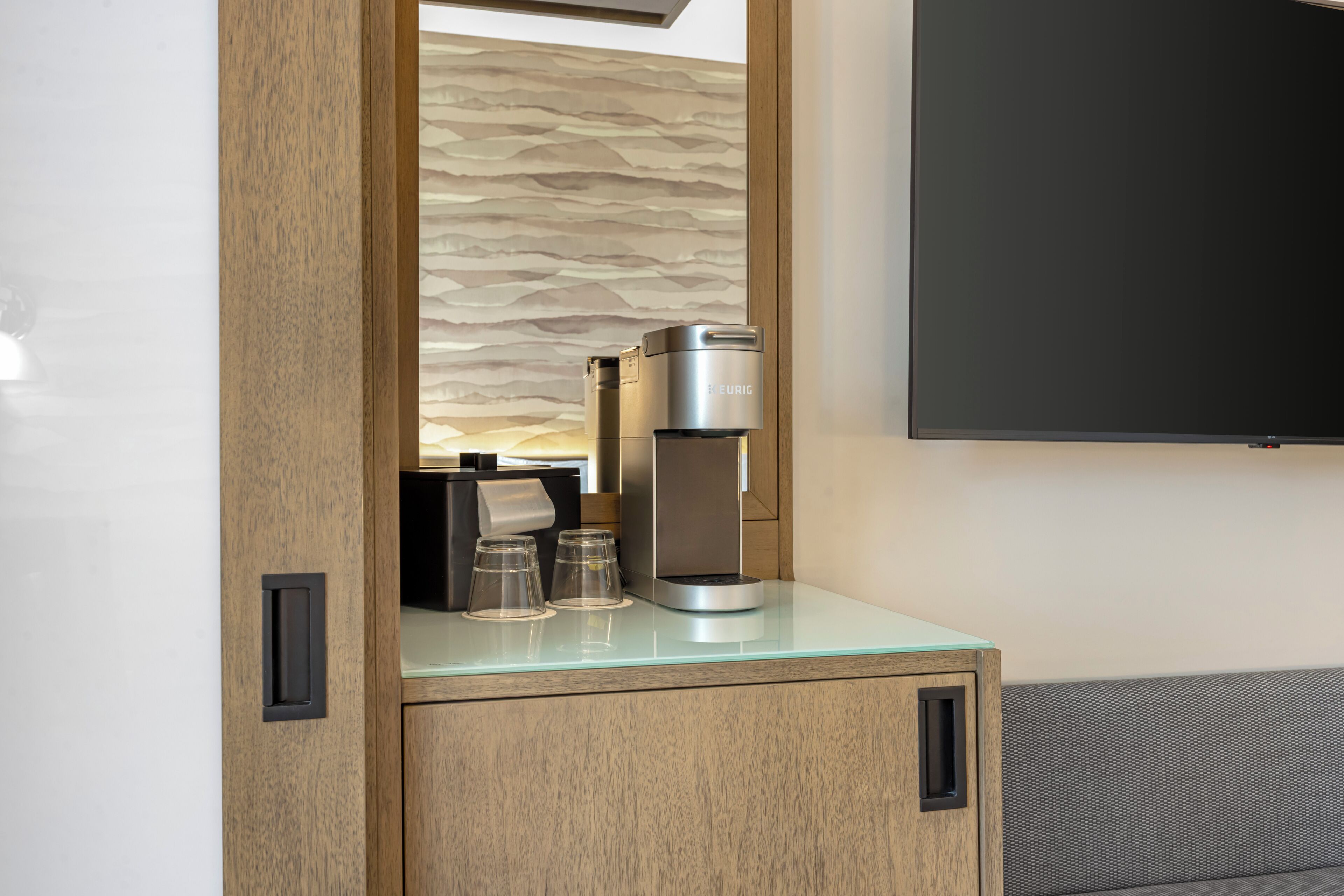 A modern kitchenette with a coffee machine, two glasses, and a small cabinet.